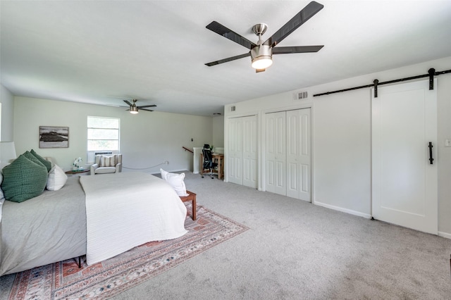 bedroom with a barn door, two closets, carpet, and ceiling fan