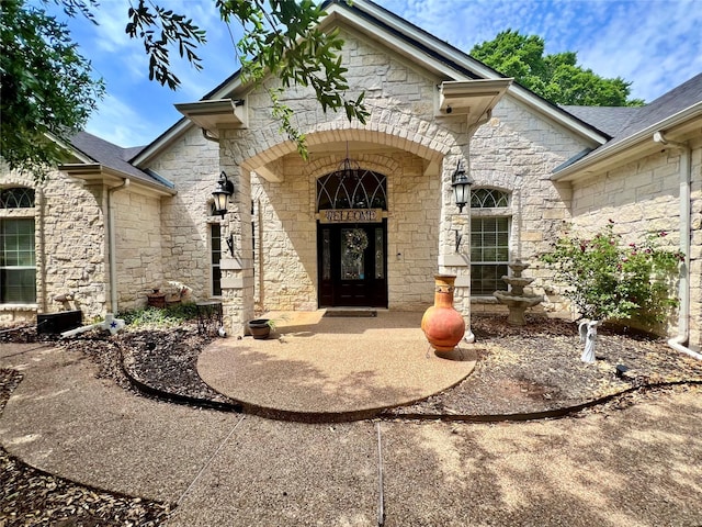 doorway to property featuring cooling unit, roof with shingles, and stone siding