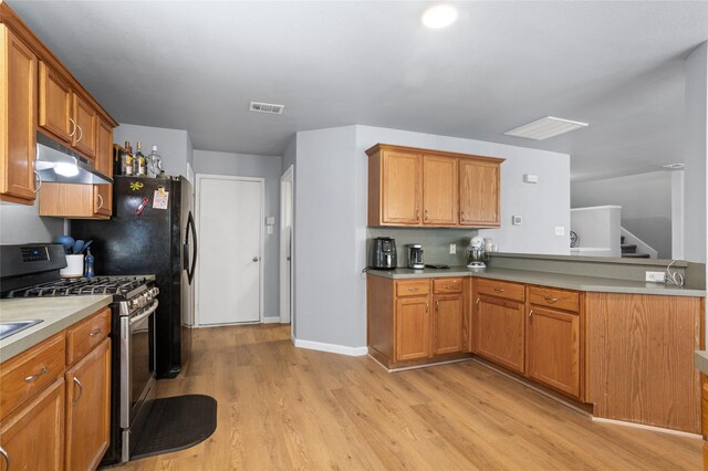 kitchen featuring brown cabinetry, visible vents, gas stove, light wood finished floors, and under cabinet range hood