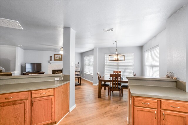 kitchen featuring visible vents, a tiled fireplace, ceiling fan with notable chandelier, and light wood-type flooring