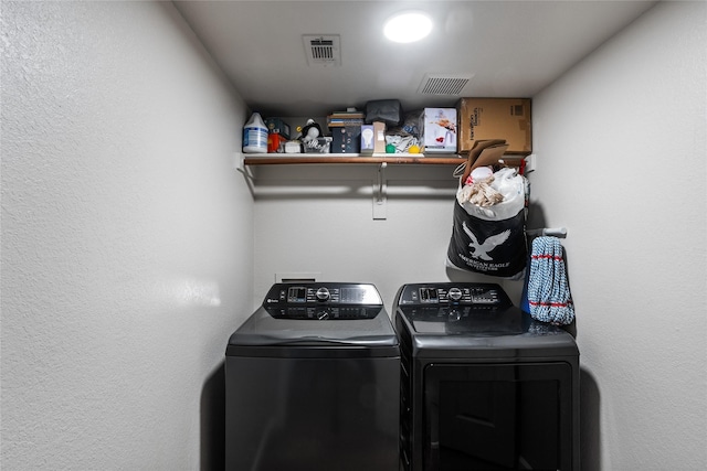 washroom with laundry area, a textured wall, washer and dryer, and visible vents
