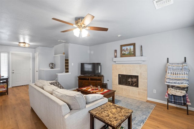 living room featuring ceiling fan, visible vents, a fireplace, wood finished floors, and baseboards