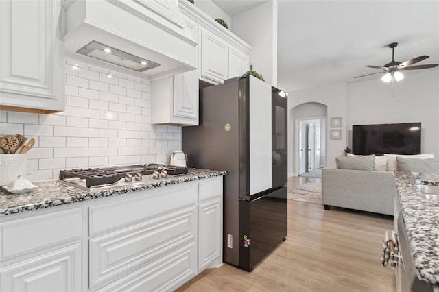 kitchen with a ceiling fan, arched walkways, freestanding refrigerator, premium range hood, and stainless steel gas cooktop