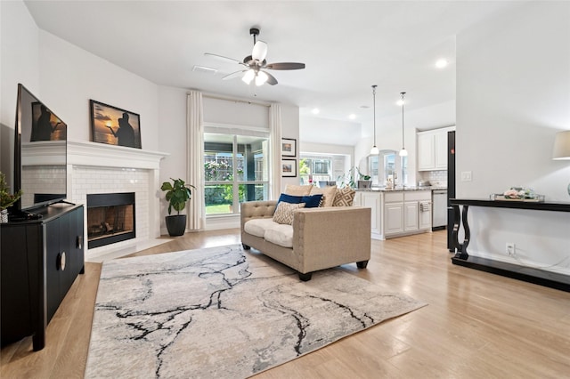 living area with a fireplace, light wood-type flooring, visible vents, and ceiling fan