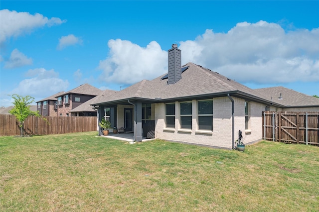 rear view of house with a fenced backyard, a chimney, a patio, and a lawn