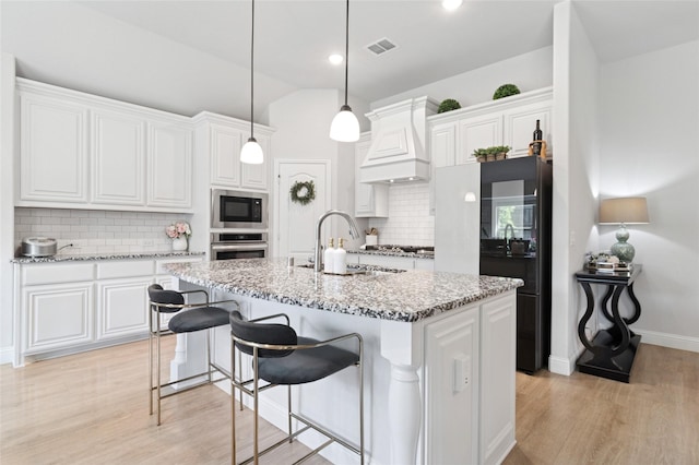 kitchen with a sink, tasteful backsplash, light wood-type flooring, visible vents, and custom range hood