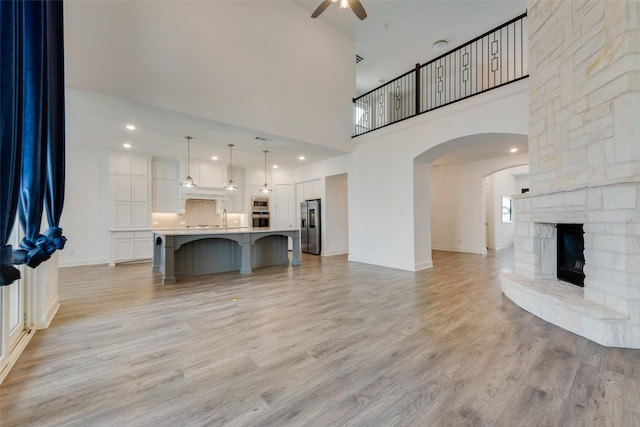4600 Paintbrush Way, Aubrey, TX 76227 - unfurnished living room with arched walkways, light wood-type flooring, a towering ceiling, ceiling fan, and a stone fireplace