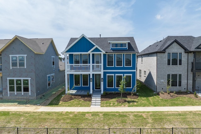 view of front facade featuring a front lawn, a balcony, a shingled roof, and fence private yard