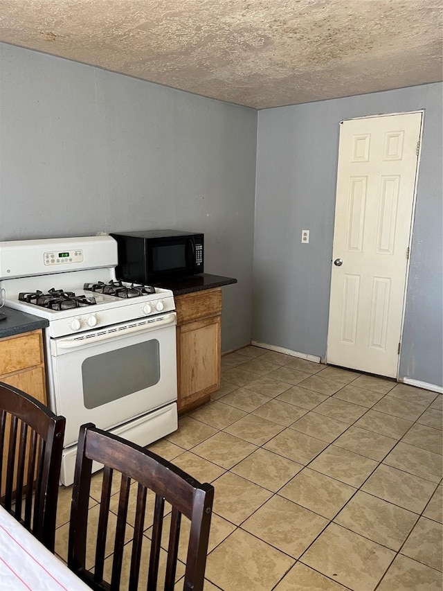 kitchen featuring a textured ceiling, dark countertops, white range with gas cooktop, black microwave, and light tile patterned floors