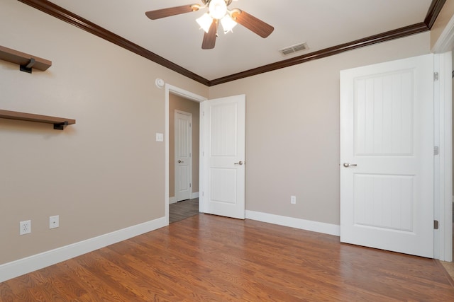 unfurnished bedroom with crown molding, wood finished floors, ceiling fan, baseboards, and visible vents