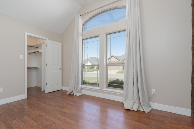 unfurnished bedroom with a spacious closet, dark wood finished floors, lofted ceiling, and baseboards