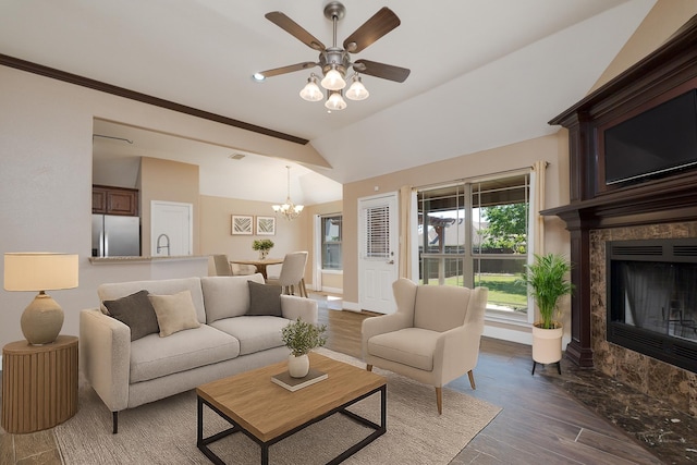 living area featuring wood finished floors, ceiling fan with notable chandelier, a tiled fireplace, baseboards, and lofted ceiling