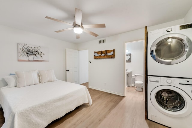 bedroom featuring light wood finished floors, stacked washer / dryer, visible vents, ensuite bath, and baseboards