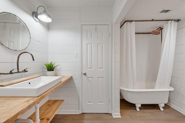bathroom with visible vents, a washtub, wood finished floors, and a sink