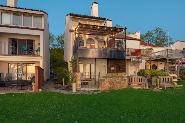 back of property with stucco siding, a lawn, a chimney, and a balcony