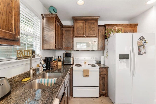 kitchen featuring recessed lighting, a sink, light tile patterned flooring, white appliances, and dark stone counters