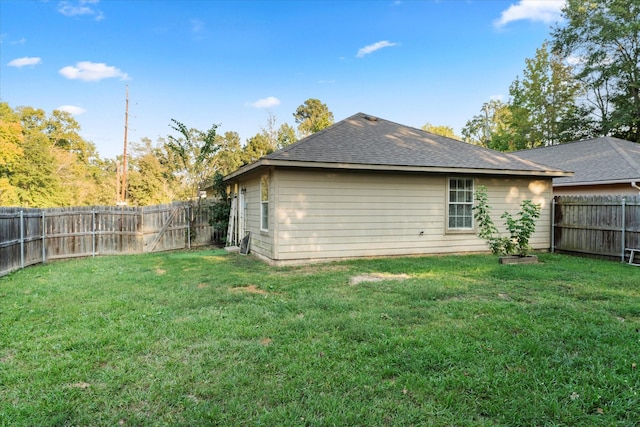 back of property with a fenced backyard, roof with shingles, and a yard