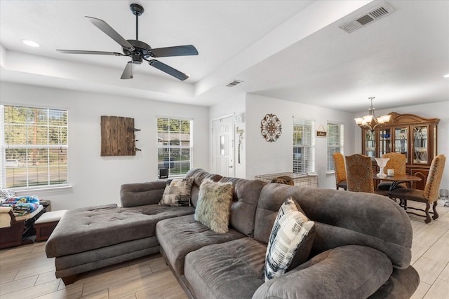living area featuring light wood-style flooring, a tray ceiling, visible vents, and ceiling fan with notable chandelier
