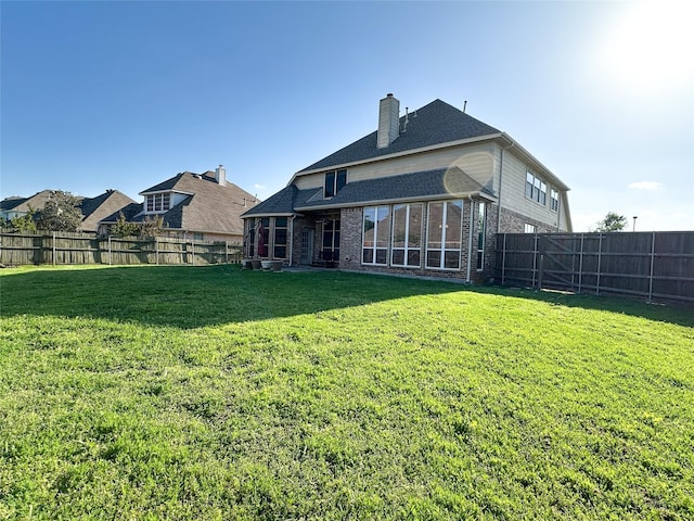 back of house with a lawn, brick siding, a chimney, and a fenced backyard