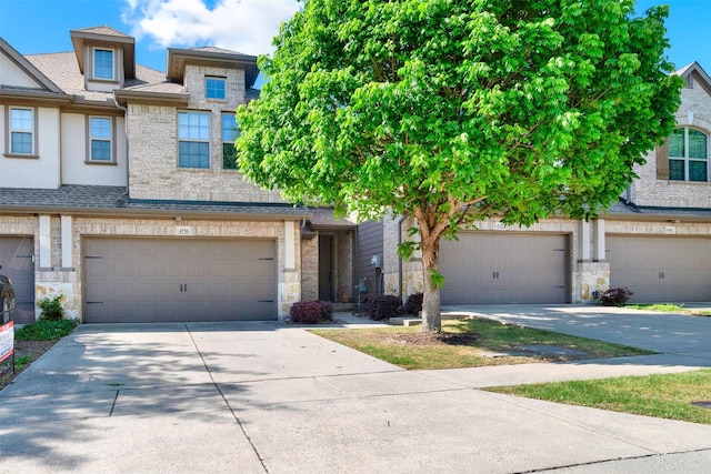 multi unit property featuring driveway, stone siding, an attached garage, brick siding, and roof with shingles