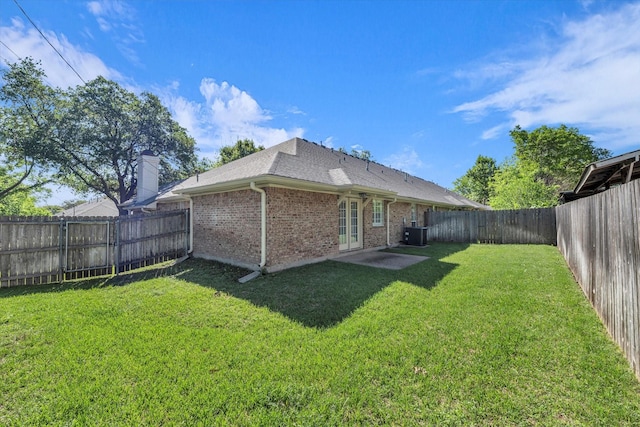 back of house with central AC unit, a shingled roof, a fenced backyard, a yard, and brick siding