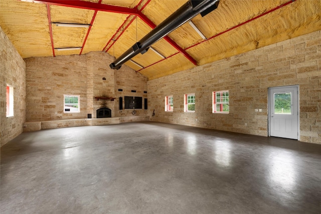 unfurnished living room with a fireplace, a wealth of natural light, finished concrete flooring, and high vaulted ceiling