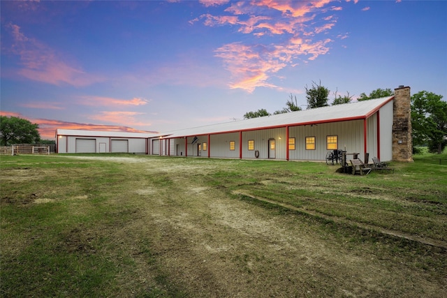 back of house at dusk featuring a garage, an outbuilding, a chimney, and metal roof