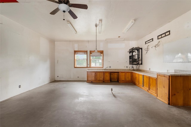 kitchen featuring a ceiling fan, concrete floors, brown cabinetry, light countertops, and decorative light fixtures