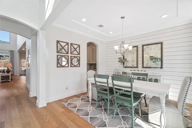 dining area featuring arched walkways, a chandelier, wood finished floors, and wooden walls