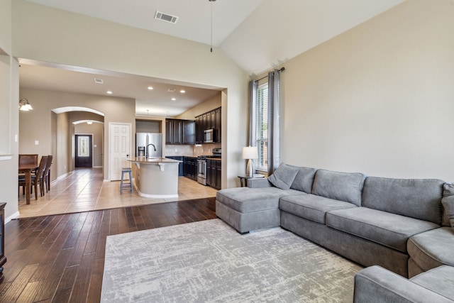 living area featuring arched walkways, vaulted ceiling, visible vents, recessed lighting, and light wood-style floors