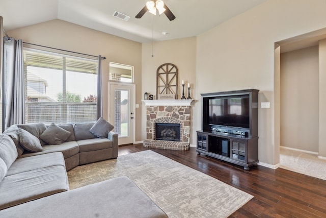 living room featuring baseboards, visible vents, a ceiling fan, a stone fireplace, and dark wood-type flooring