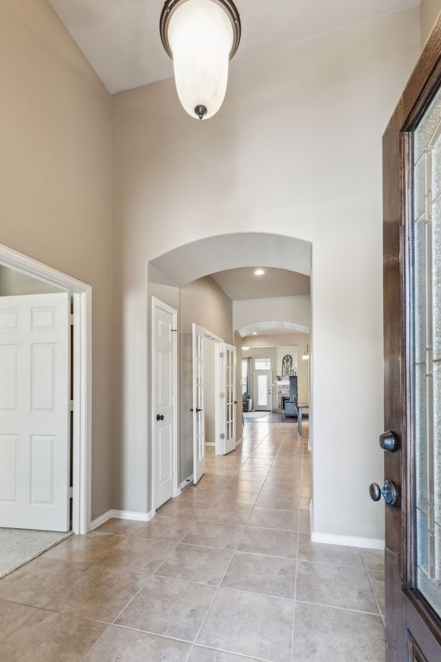 entrance foyer with french doors, arched walkways, a towering ceiling, baseboards, and light tile patterned floors
