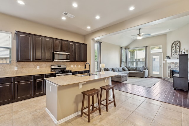 kitchen with stainless steel appliances, a sink, open floor plan, visible vents, and a kitchen bar