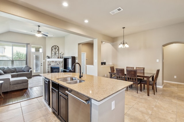 kitchen with stainless steel dishwasher, a sink, arched walkways, a fireplace, and open floor plan