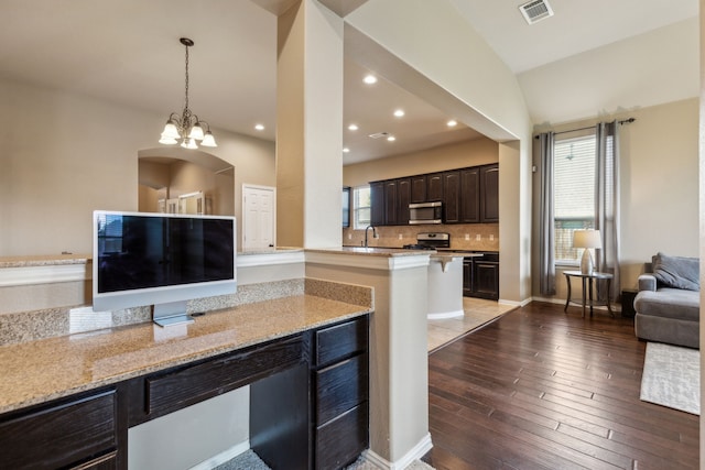 kitchen with hardwood / wood-style floors, light stone counters, stainless steel appliances, dark brown cabinets, and visible vents