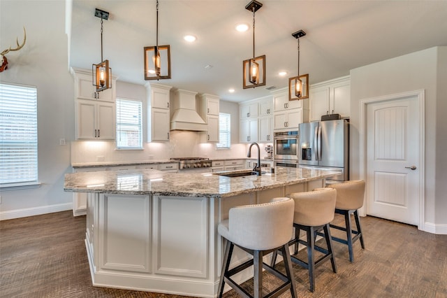 kitchen featuring backsplash, a sink, a kitchen island with sink, appliances with stainless steel finishes, and white cabinetry
