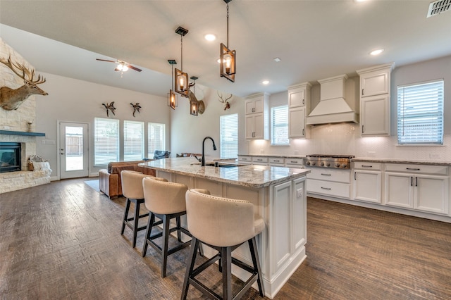 kitchen with a sink, stainless steel gas cooktop, open floor plan, custom range hood, and visible vents