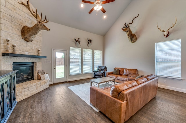 living room featuring high vaulted ceiling, a ceiling fan, a stone fireplace, wood finished floors, and baseboards