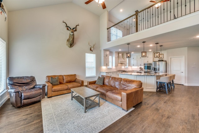 living room featuring high vaulted ceiling, ceiling fan, a healthy amount of sunlight, baseboards, and dark wood-type flooring