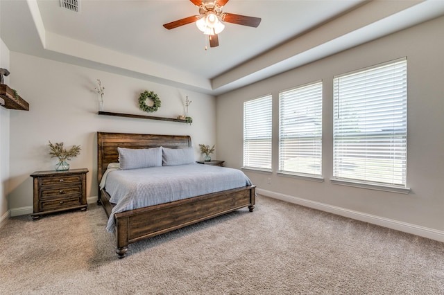 carpeted bedroom featuring ceiling fan, baseboards, a tray ceiling, and visible vents