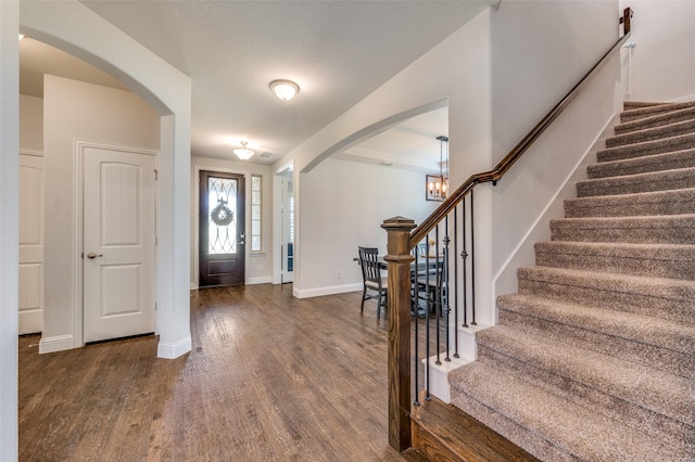 entrance foyer featuring arched walkways, stairs, and dark wood-type flooring