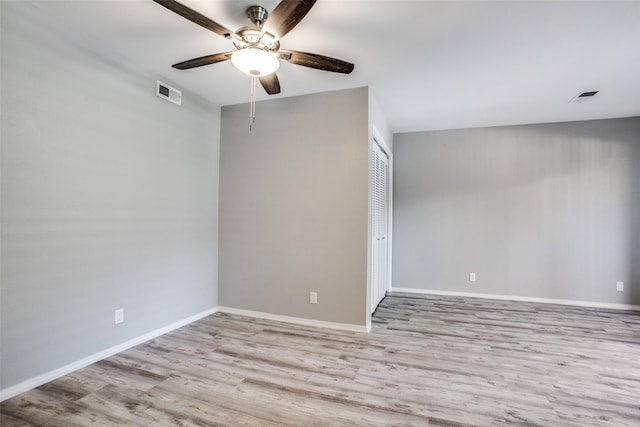spare room with wood finished floors, visible vents, a ceiling fan, and baseboards