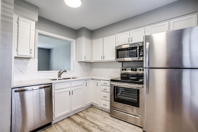 kitchen with a sink, light wood-style floors, stainless steel appliances, light countertops, and white cabinets