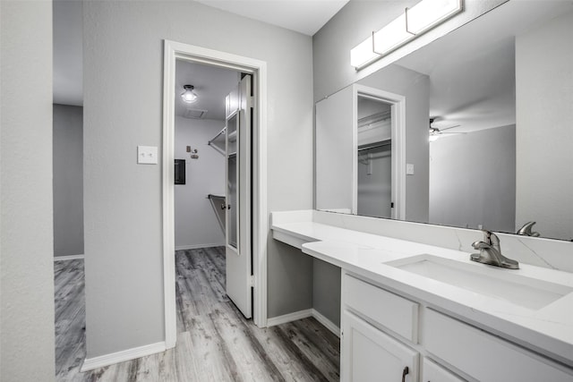 bathroom featuring a ceiling fan, wood finished floors, a spacious closet, and vanity