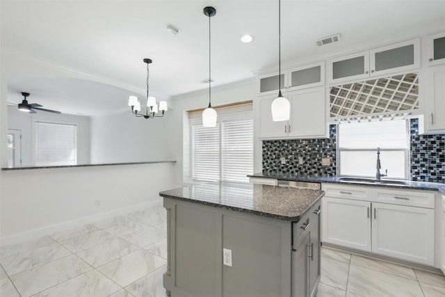 kitchen featuring a center island, dark stone countertops, a sink, ceiling fan with notable chandelier, and backsplash