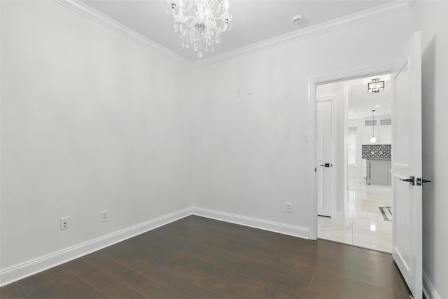 empty room with wood finished floors, baseboards, ornamental molding, and an inviting chandelier