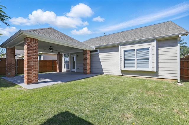 rear view of property with a ceiling fan, fence, a shingled roof, a patio area, and a lawn
