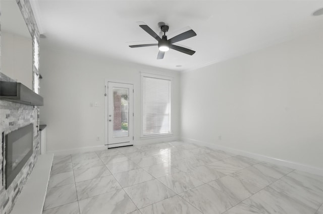 unfurnished living room with a stone fireplace, marble finish floor, baseboards, and a ceiling fan