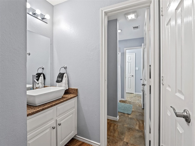 bathroom featuring stone finish floors, vanity, and baseboards