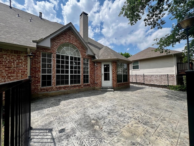 rear view of property featuring brick siding, a patio area, fence, and a chimney